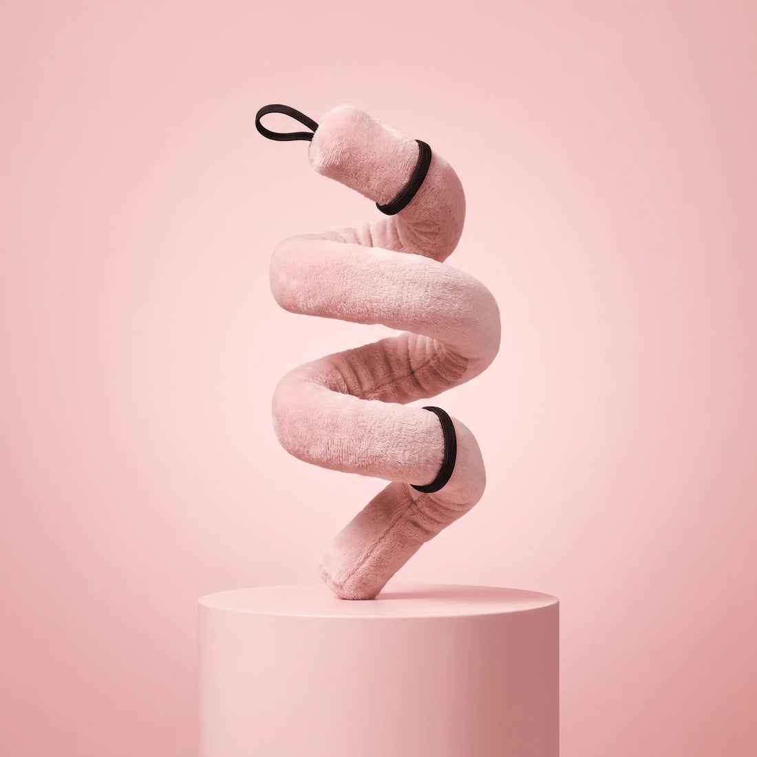 Soft pink heatless curler with black elastic bands, styled in spiral on pedestal for salon-worthy curls